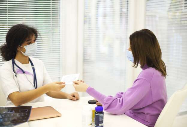 African-american woman doctor wearing face mask giving CD with X-ray