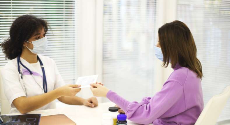African-american woman doctor wearing face mask giving CD with X-ray